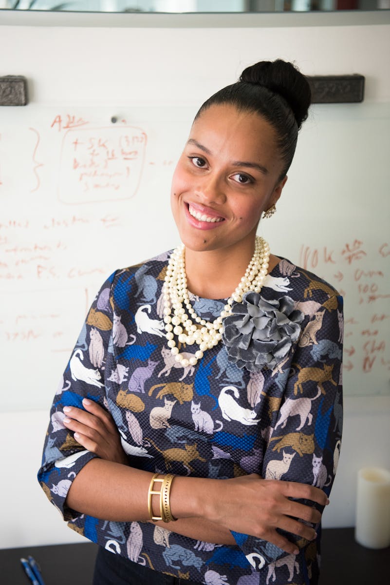 Smiling businesswoman in stylish outfit against office whiteboard backdrop.