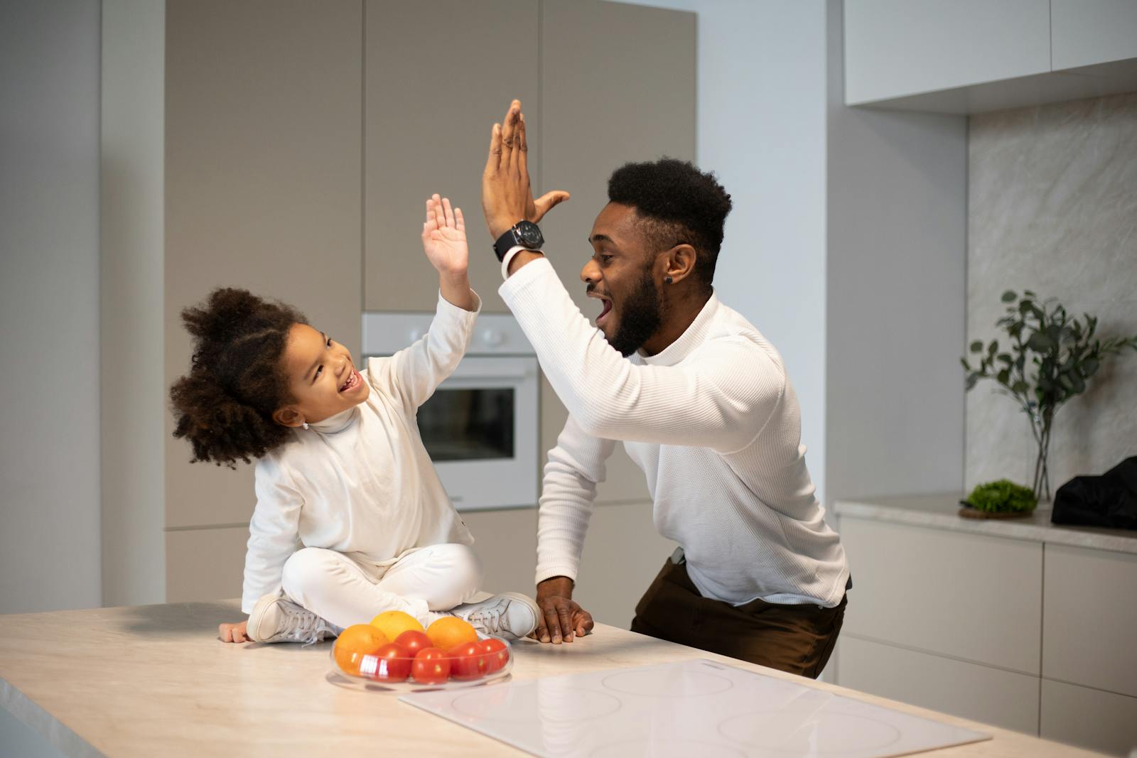 Playful moment between father and daughter sharing a high five in a modern kitchen.