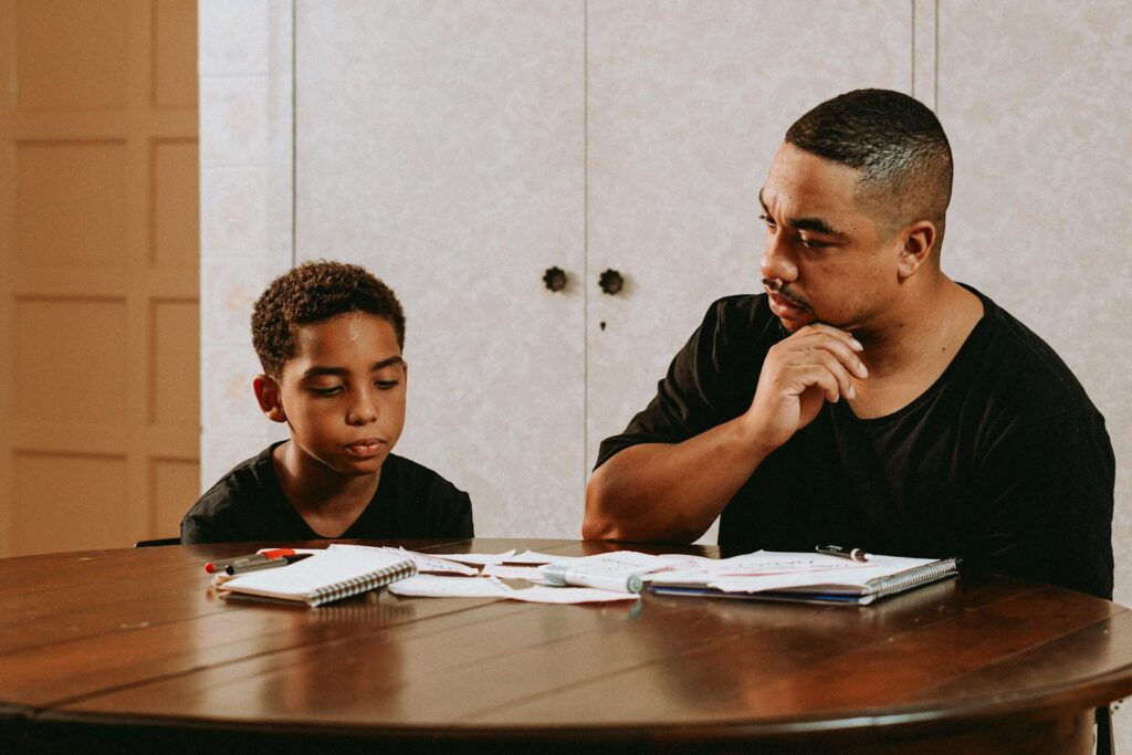 A father helps his son with homework at a table, fostering learning and connection.