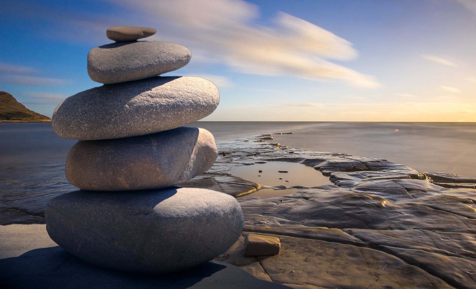 A serene stack of stones on the rocky seashore during a peaceful sunrise, embodying balance and zen.