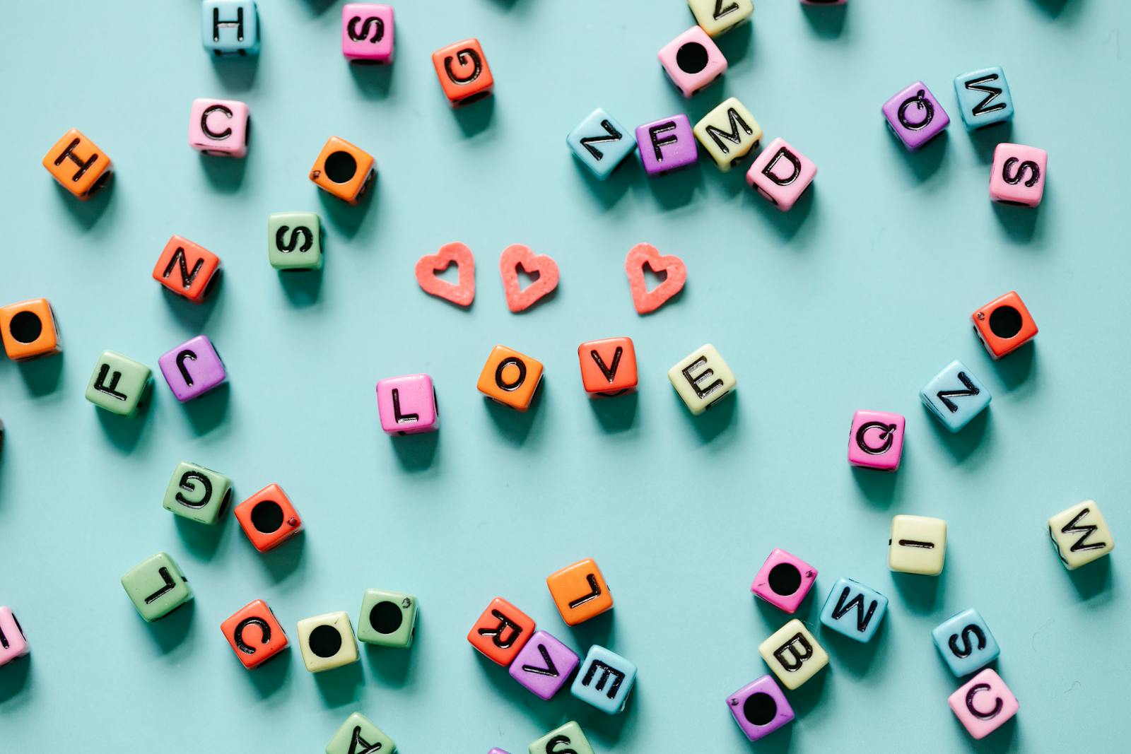 Colorful alphabet dice spelling 'LOVE' on a blue background with heart shapes.