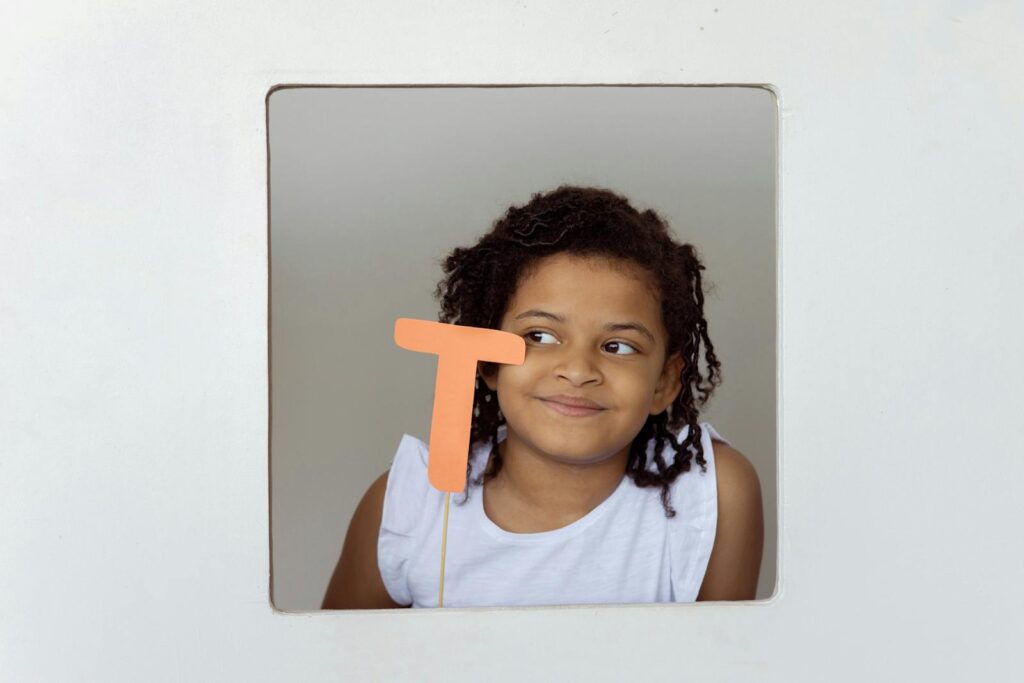 Creative portrait of a child smiling while holding a paper letter T, showcasing creativity and art.