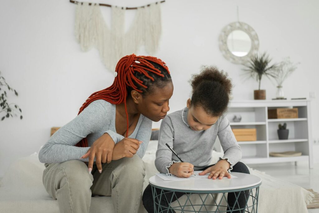 A mother helps her daughter with homework at a stylish indoor setting. The scene is warm and educational.