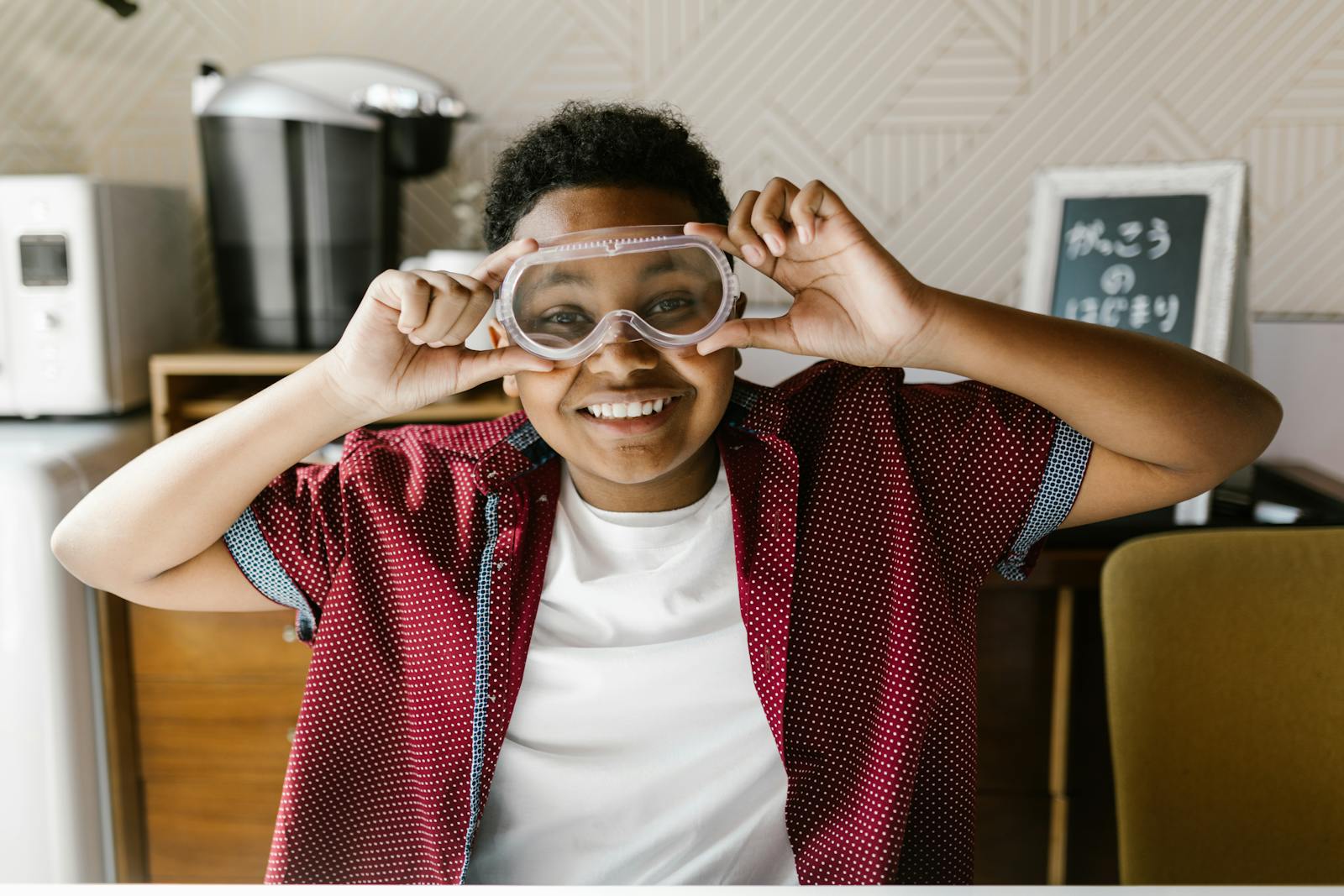 A cheerful boy wearing goggles indoors, partaking in a school project.